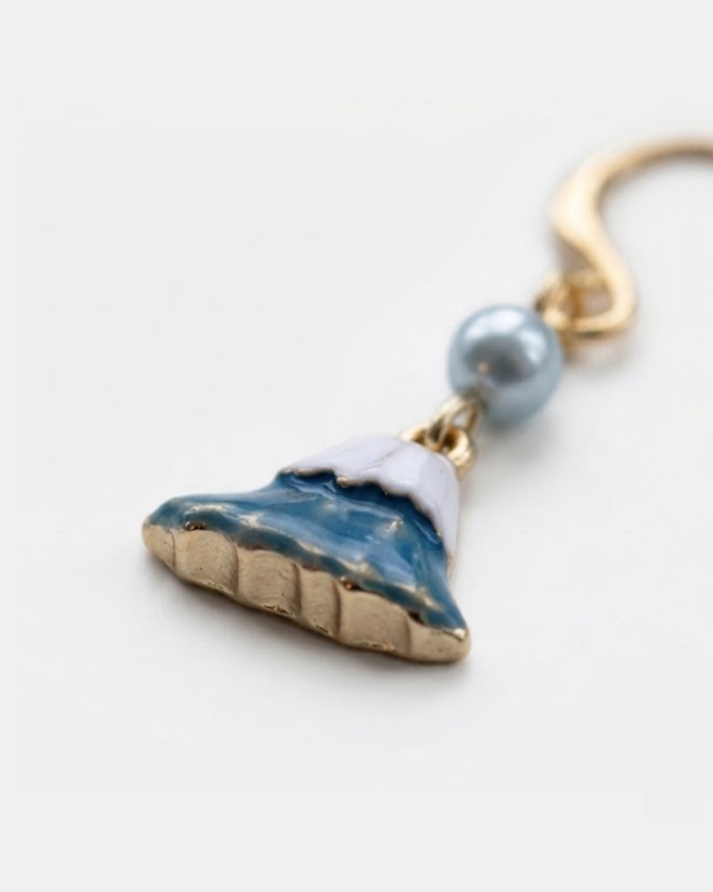 Close up shot of a gold earring with charm of mt fuji and light blue pearl