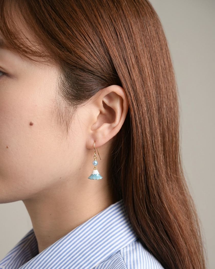 Model wearing a pair of gold earring with charm of mt fuji and light blue pearl