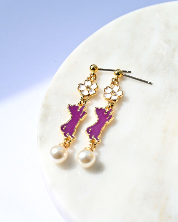 Purple cat-shaped earrings with gold accents on a white surface