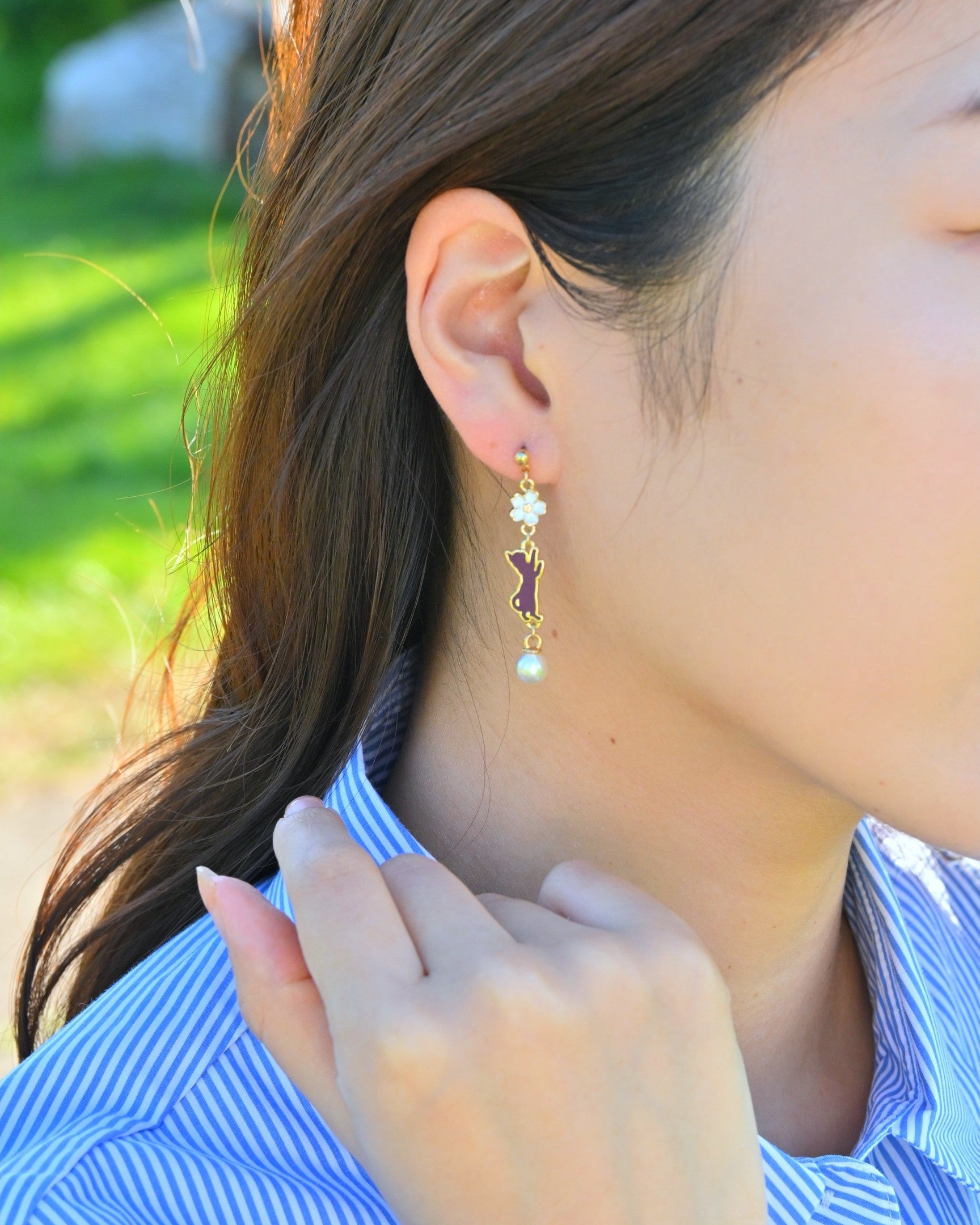 A model wearing a earring with cat and white cherry blossom charm.