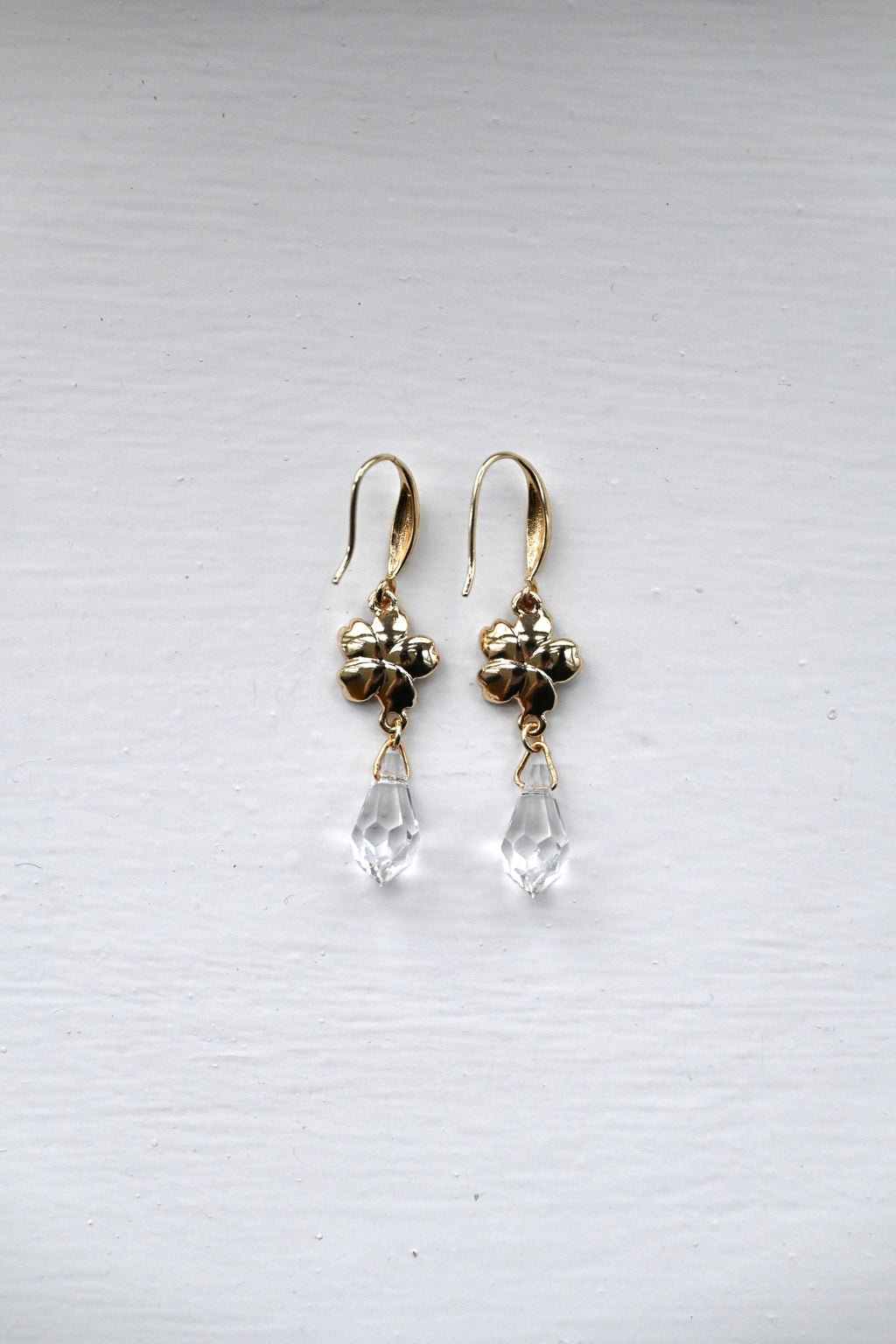 Gold earrings with  sakura charms and clear teardrop beads on a white surface.