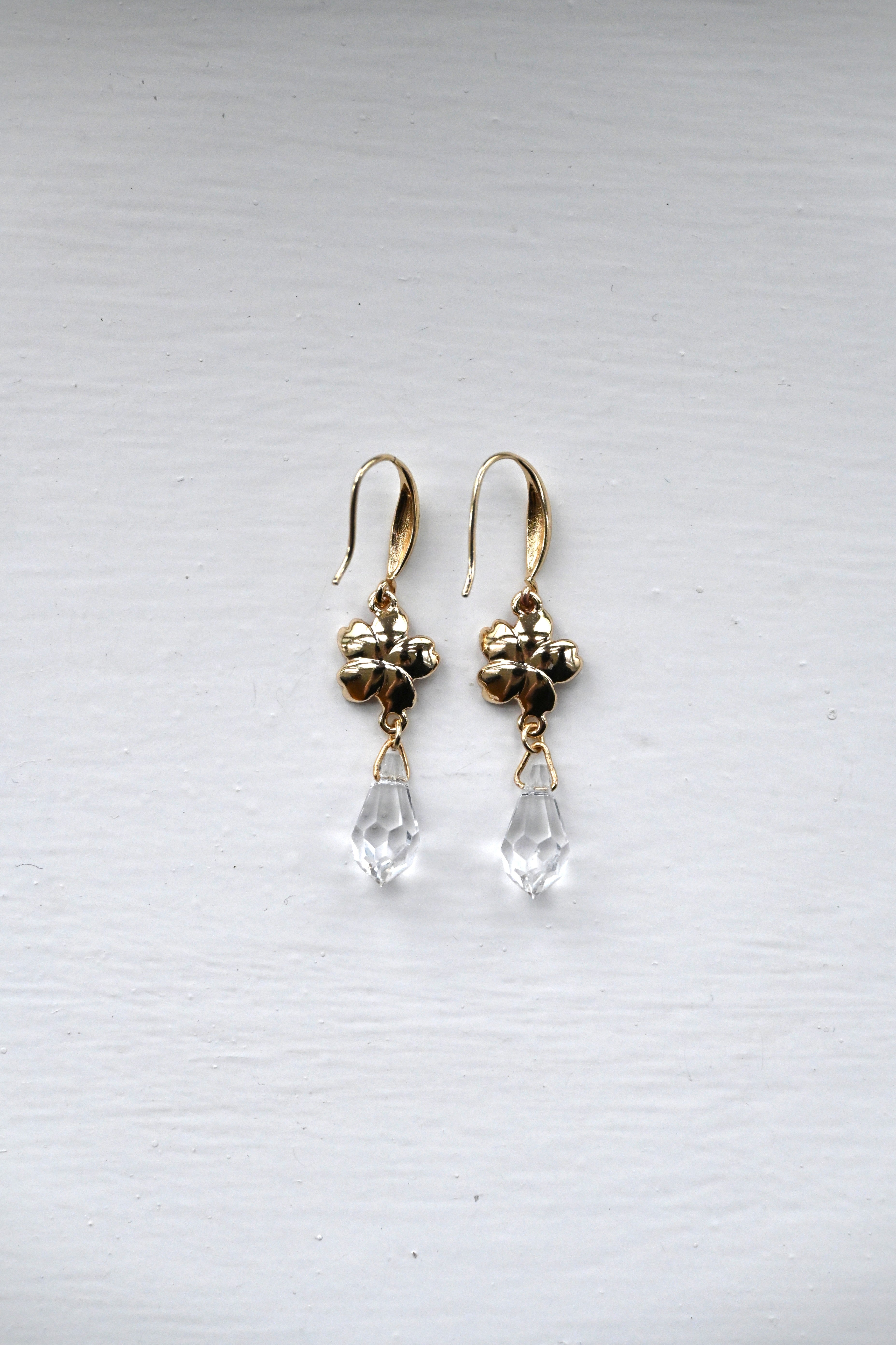 Gold earrings with  sakura charms and clear teardrop beads on a white surface.