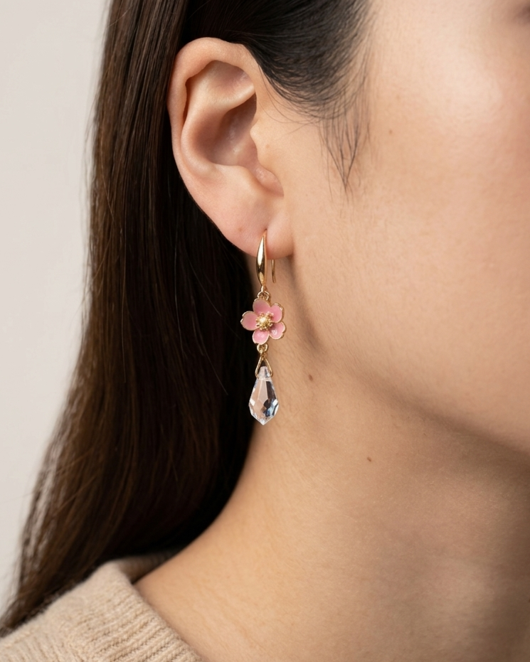 Close-up of an ear wearing a floral earring with a clear teardrop pendant.