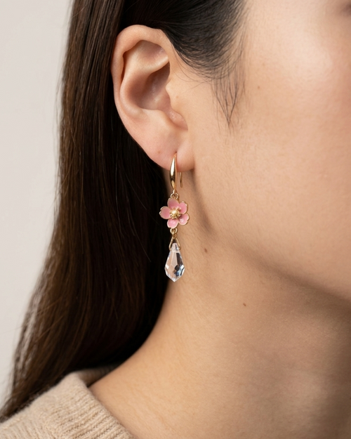 Close-up of an ear wearing a floral earring with a clear teardrop pendant.
