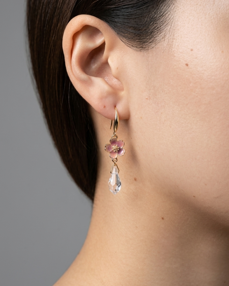 Model wearing gold earrings with pink sakura charms and clear teardrop beads.