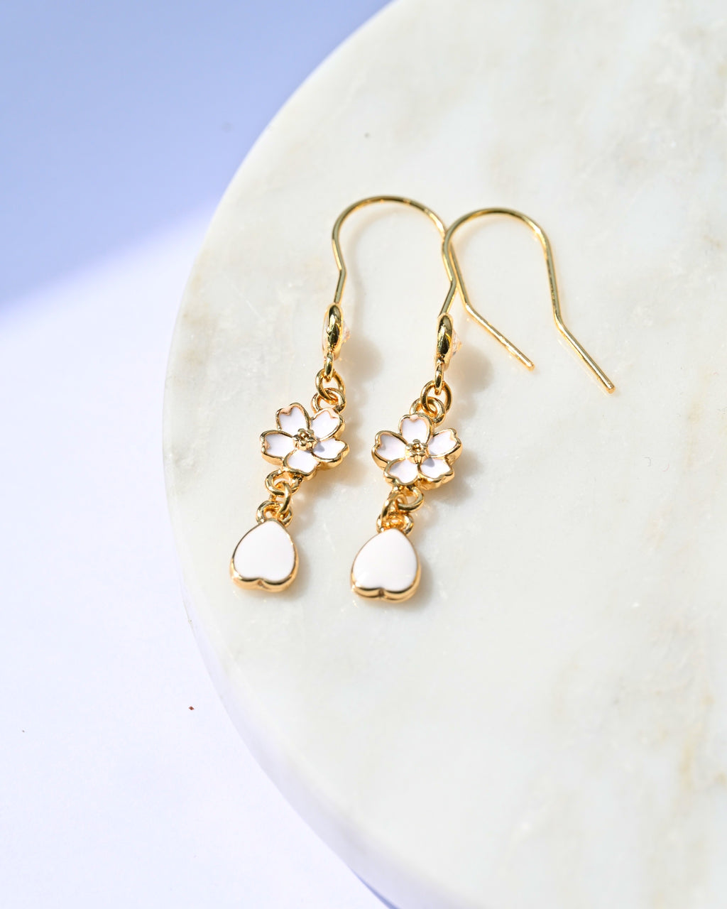 Gold earrings with heart and flower designs on a white surface
