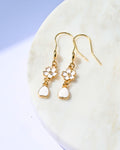 Gold earrings with heart and flower designs on a white surface