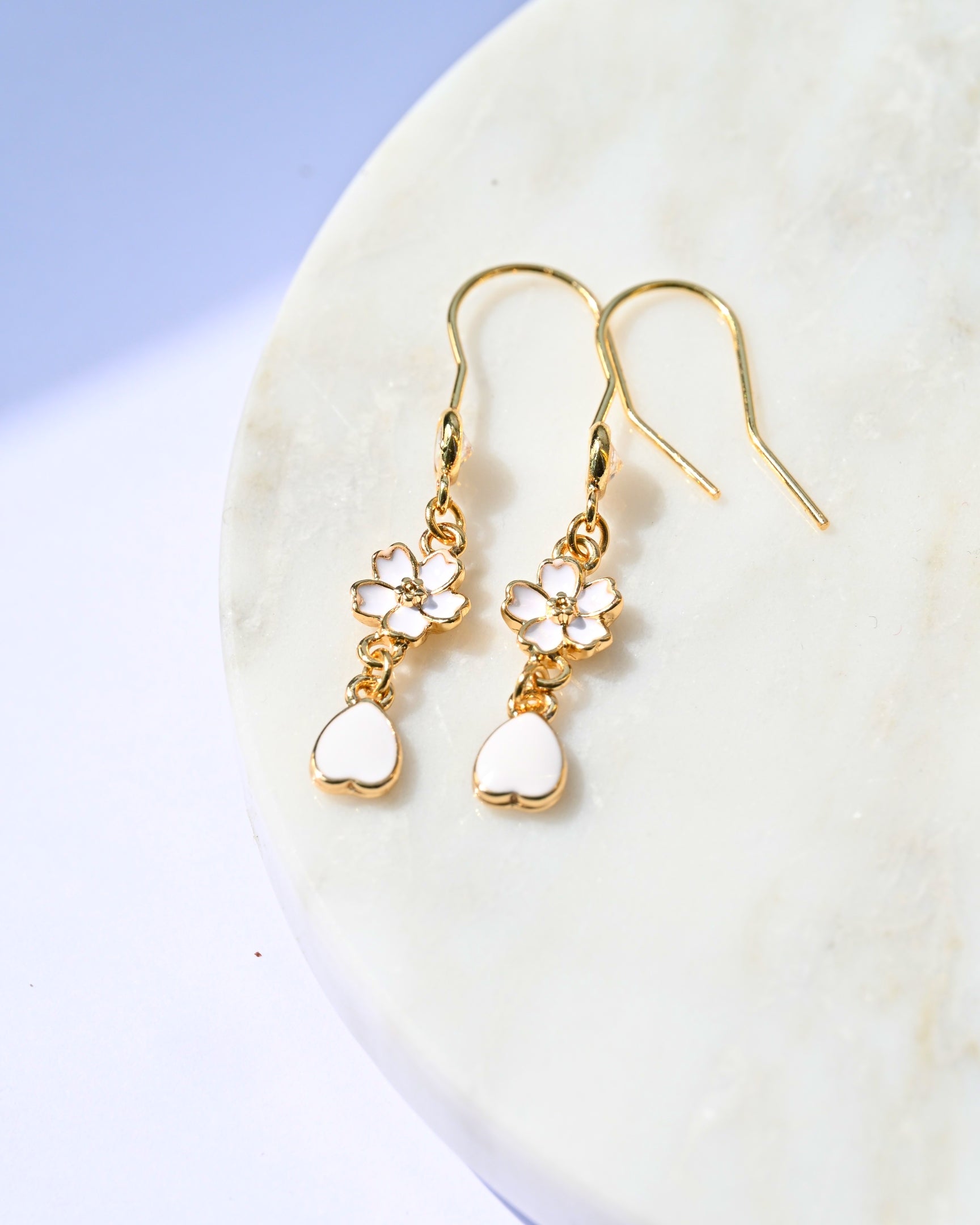 Gold earrings with heart and flower designs on a white surface