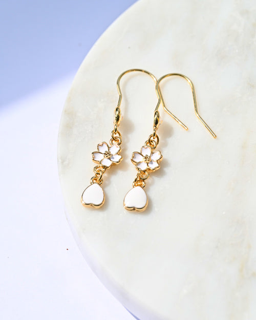 Gold earrings with heart and flower designs on a white surface