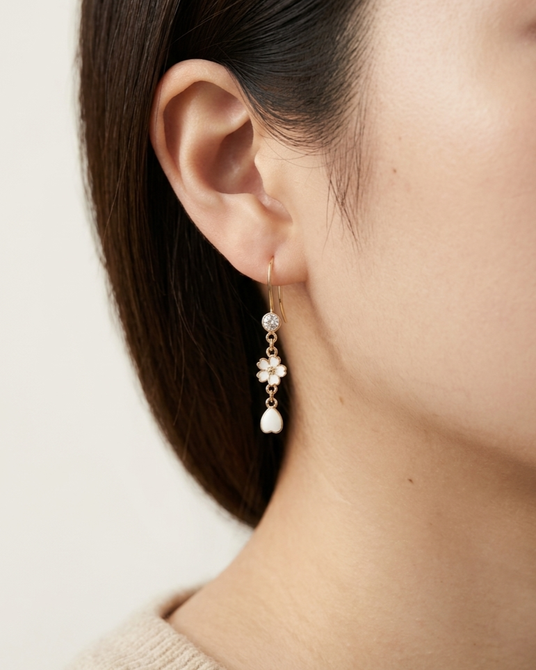 Model wearing an earring with white sakura flower and petal charms with crystal accent.
