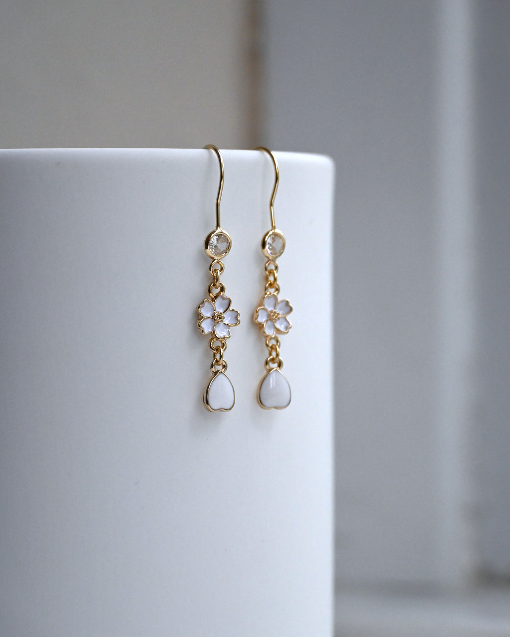 Product image of an earring with white sakura flower and petal charms against a white wall