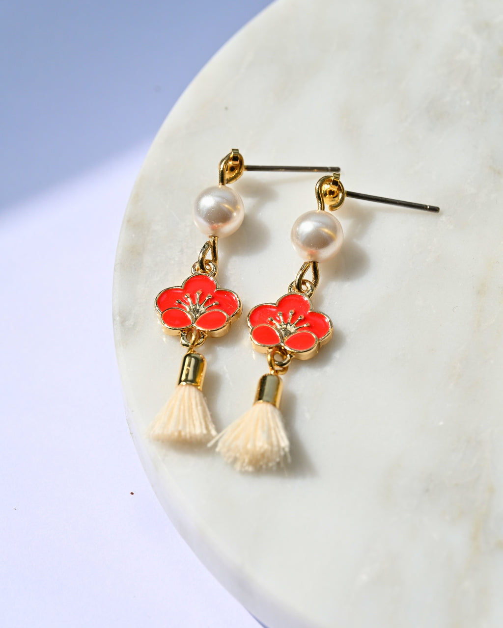 Earrings with red floral designs and white tassels on a marble surface