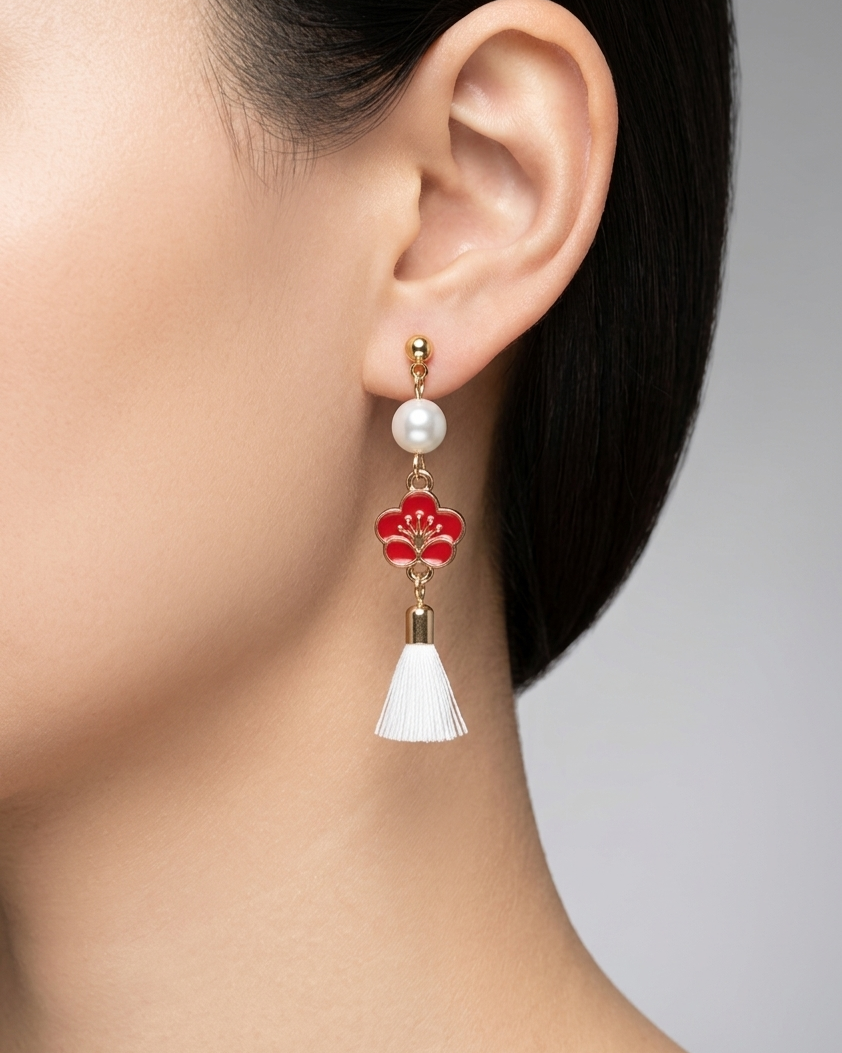 Model wearing an earring with a red plum flower design with white pearl and white tassel on a neutral background