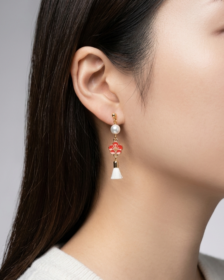 Model wearing an earring with red plum flower design with white pearl and white tussel in a white background